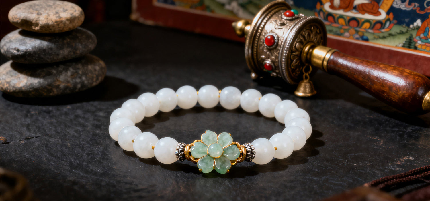 White beaded bracelet with a floral clasp on a dark surface with stones and a prayer wheel in the background.