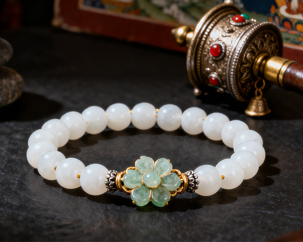 White beaded bracelet with a green floral clasp on a dark surface, with a traditional prayer wheel in the background.