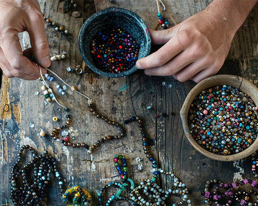Hands working with beads and jewelry on a wooden surface